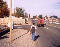 A pedestrian walking against traffic on an unpaved shoulder.